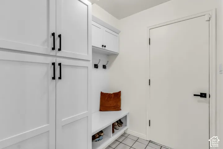Built-in white cabinetry with matte black hardware, integrated bench seating, wall-mounted hooks, and tiled flooring