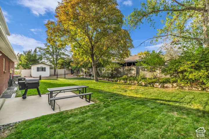 Expansive grass lawn, mature trees, concrete patio, brick exterior, and a detached shed