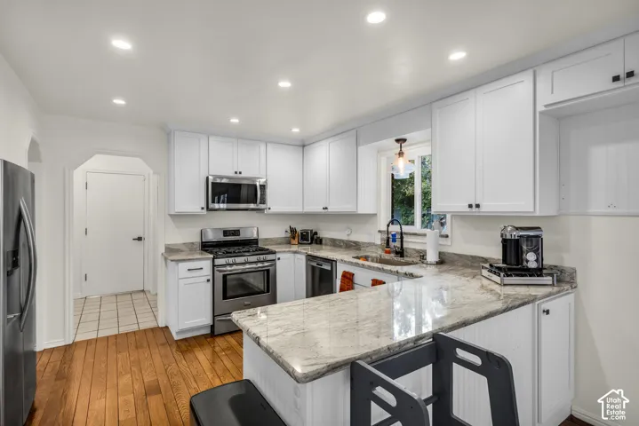 White shaker cabinetry, stainless steel appliances, recessed ceiling lighting, light-toned stone countertops, and wood-finish flooring