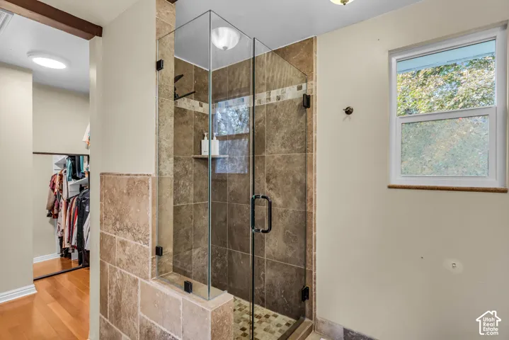 Glass-enclosed shower with stone tile surround, mosaic tile shower floor, and built-in shower shelf