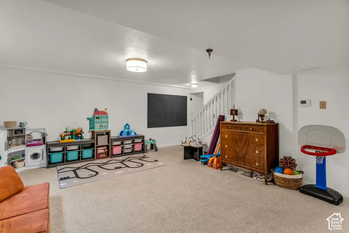 Expansive carpeted room featuring white walls, recessed ceiling lights, and a staircase with white railings