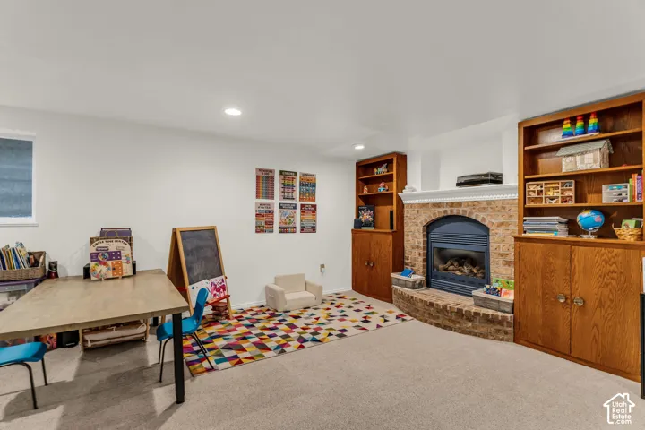 Recessed lighting, light-toned carpet, a gas fireplace with a brick surround, and built-in wood cabinetry