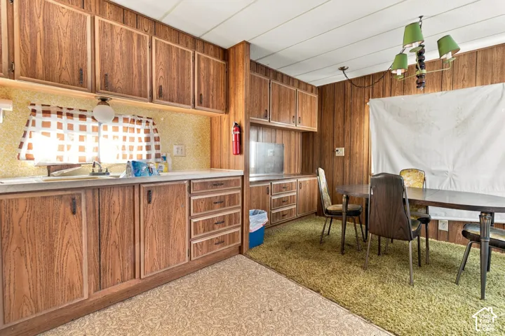 Kitchen and dining area featuring wood-finish cabinetry, a single basin sink, a wall-mounted light fixture, and textured flooring