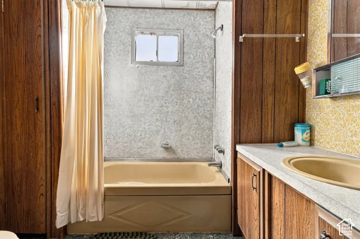 Bathtub with shower fixture, vanity with integrated sink, wood-finish cabinetry, and wall-mounted medicine cabinet