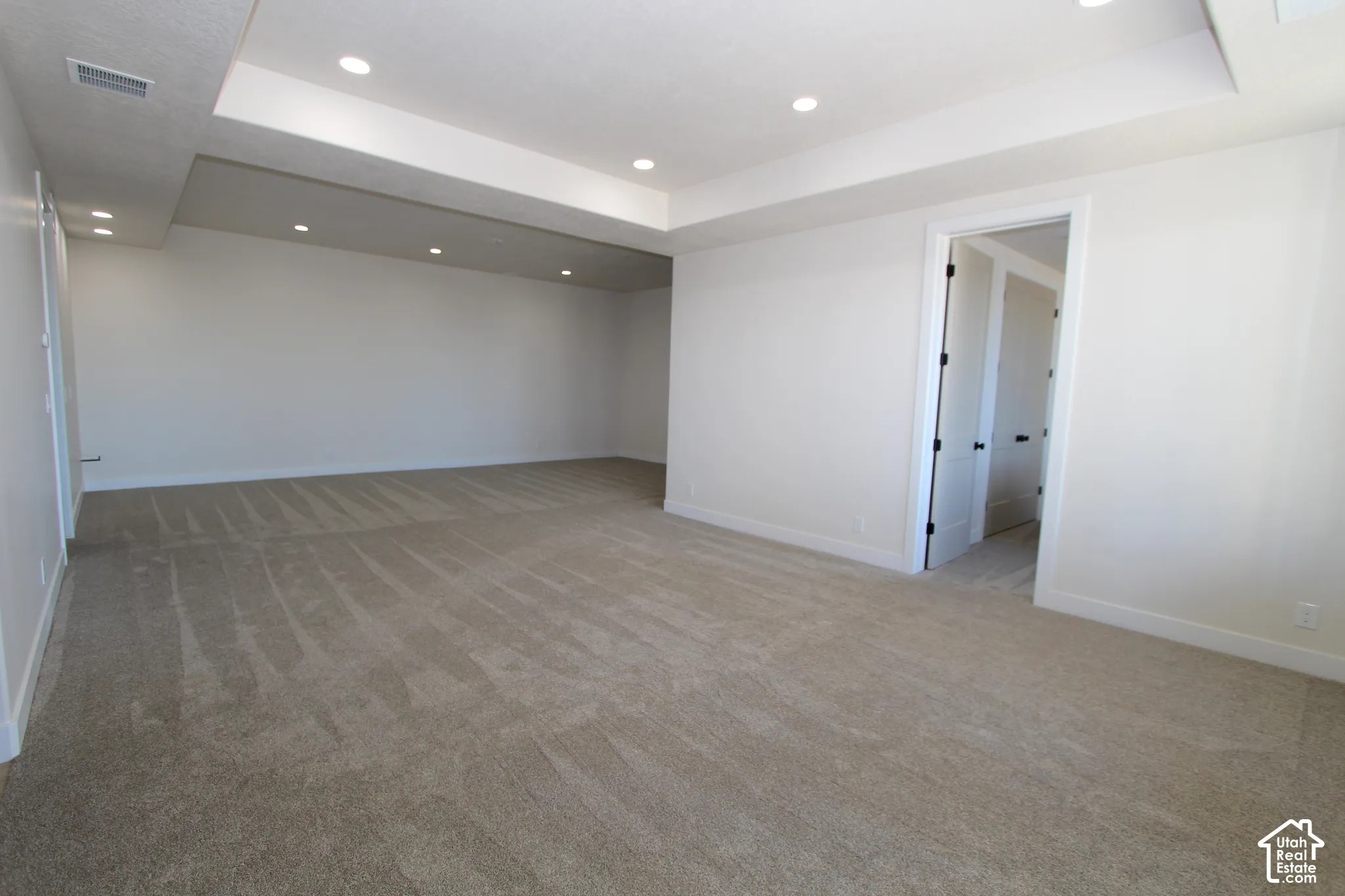 Expansive room featuring recessed lighting, tray ceiling, and neutral carpeting