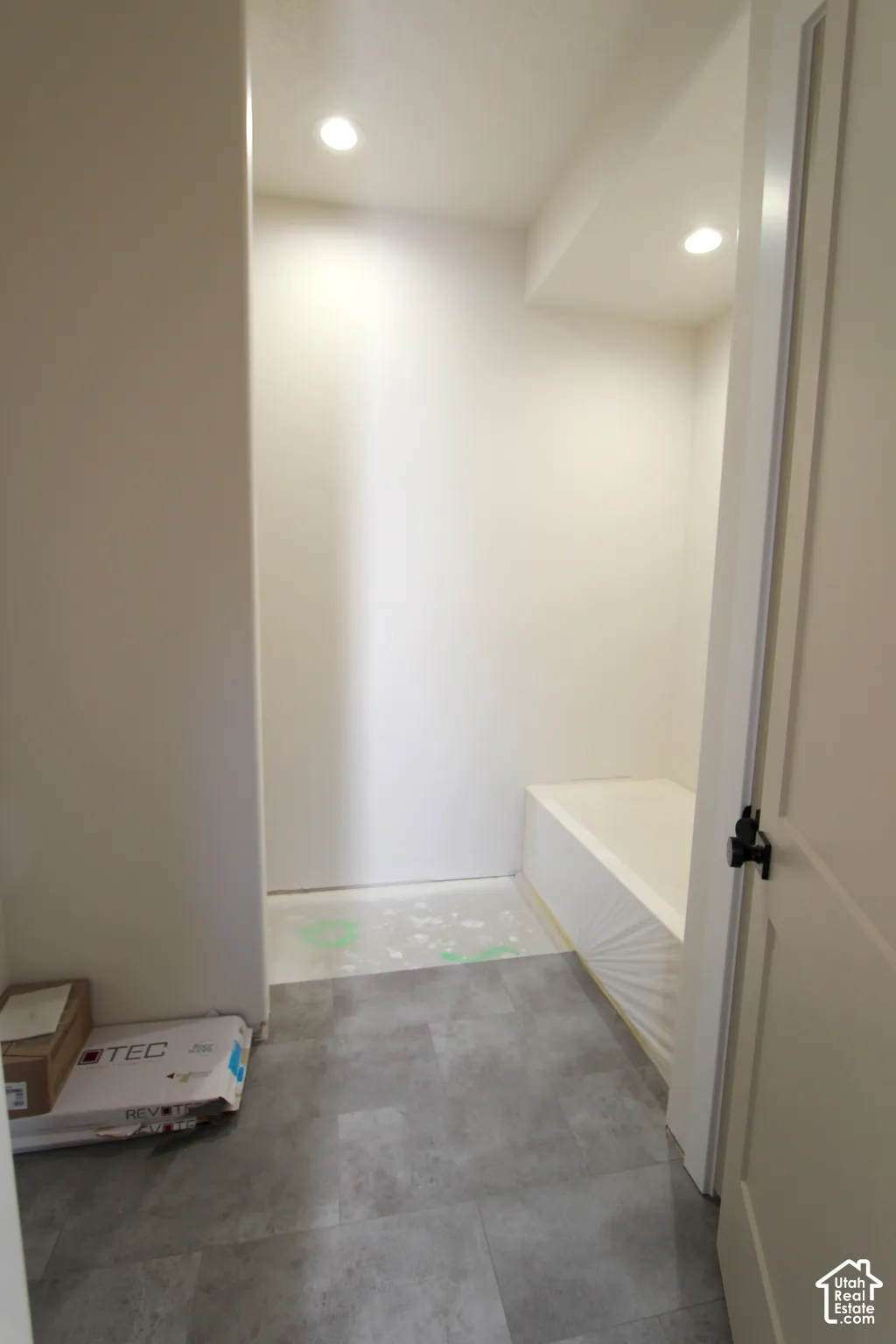 Recessed lighting, gray-toned flooring, white walls, and a white door with dark hardware
