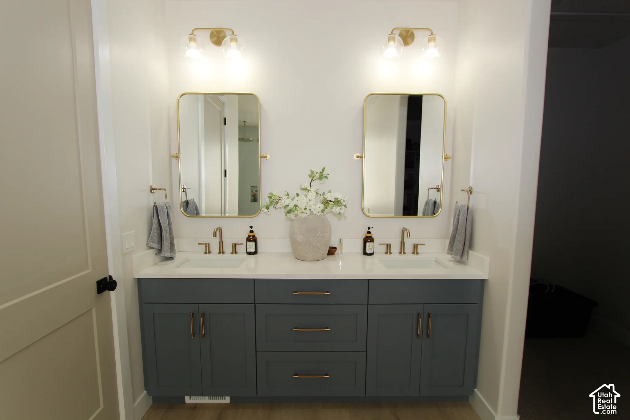 Dual gold-framed mirrors, dual wall-mounted gold light fixtures, and a dual-sink vanity with gray cabinetry