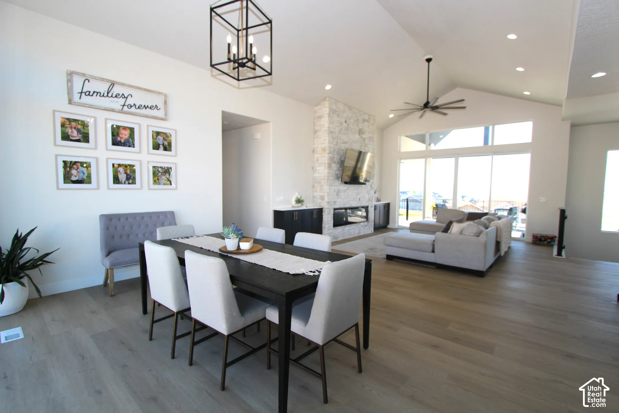 Vaulted ceilings with recessed lighting, wood-finish flooring, full-height stone fireplace with a built-in media center, large format sliding glass doors, and a linear chandelier