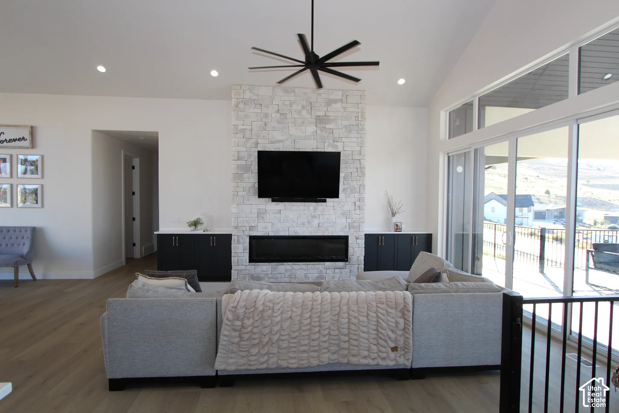 Great room featuring vaulted ceilings, wood-finish flooring, a stone-faced fireplace, built-in cabinetry, and large sliding glass doors