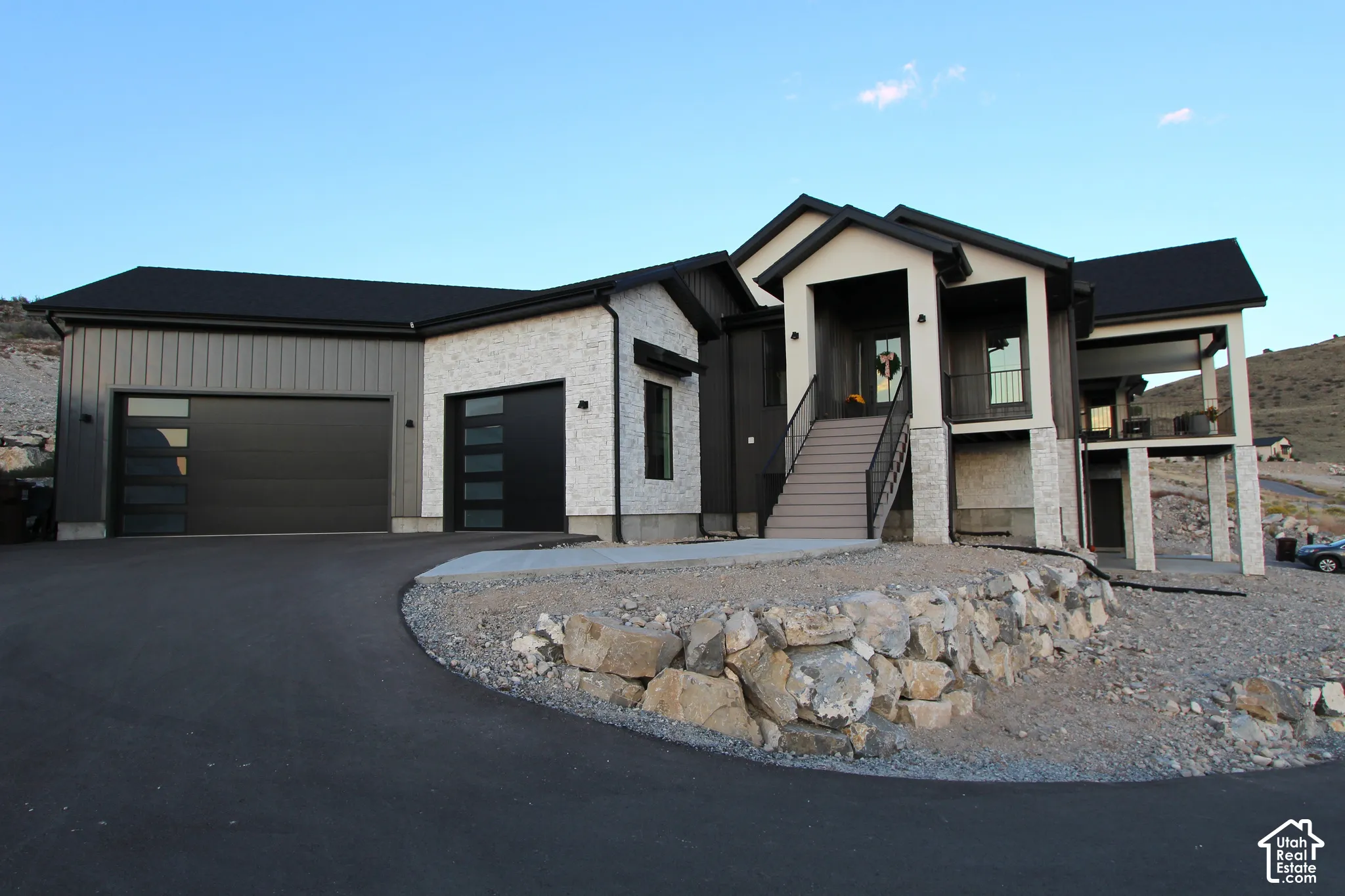 Contemporary exterior with a black roof, stone accents, two-car garage with modern doors, and a covered balcony