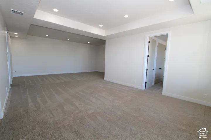 Expansive room featuring recessed lighting, tray ceiling, and neutral carpeting
