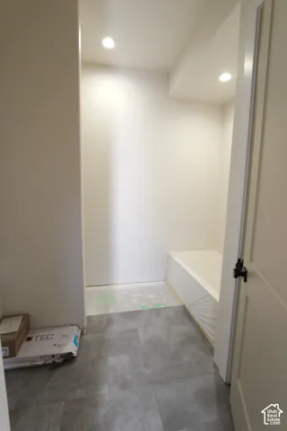 Recessed lighting, gray-toned flooring, white walls, and a white door with dark hardware