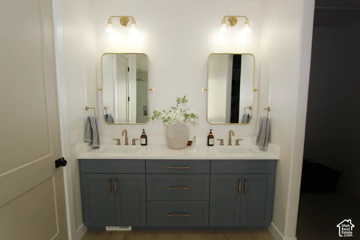 Dual gold-framed mirrors, dual wall-mounted gold light fixtures, and a dual-sink vanity with gray cabinetry