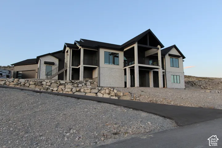 Exterior with a mix of light-colored stone and smooth siding, multiple balconies with dark railings, a dark-pitched roofline, and an attached garage with a dark sectional door