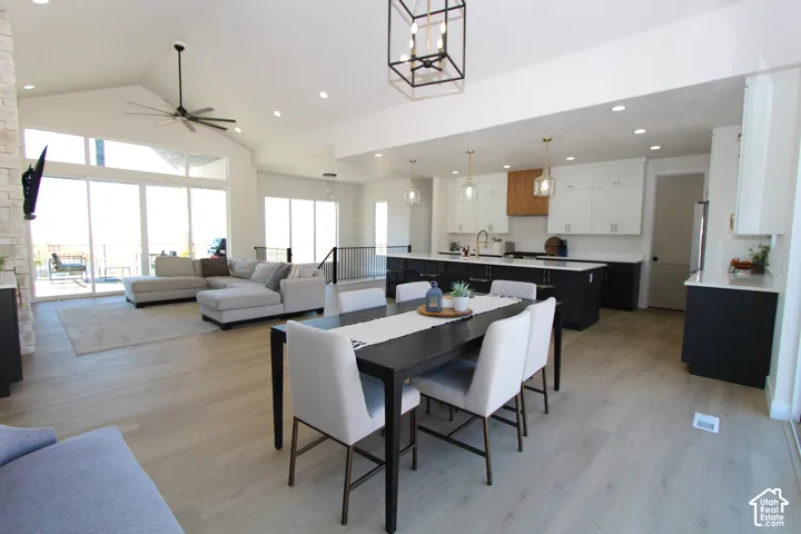 Vaulted ceiling with a contemporary ceiling fan, expansive sliding glass doors, light wood-finish flooring, and a kitchen featuring a large island with dark cabinetry and white upper cabinetry