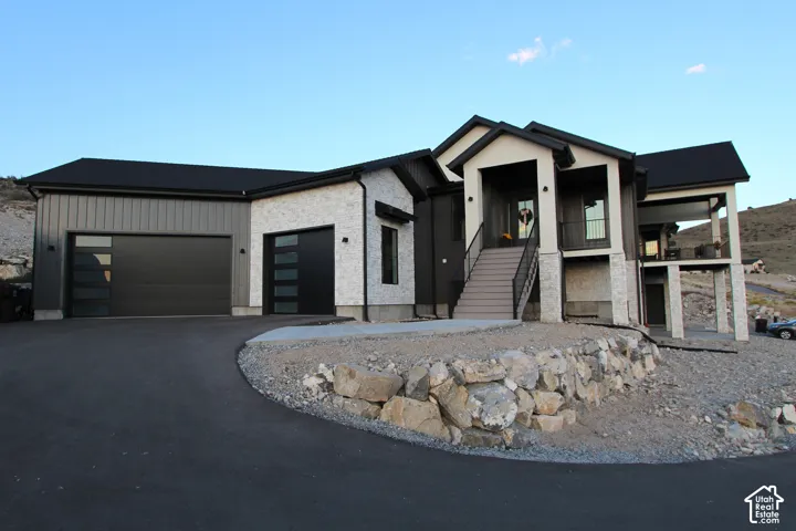 Contemporary exterior with a black roof, stone accents, two-car garage with modern doors, and a covered balcony