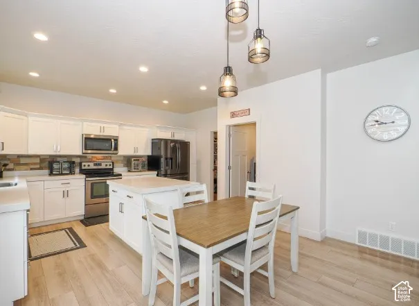Recessed ceiling lighting, wood-finish flooring, white cabinetry with dark hardware, stainless steel appliances, and a central kitchen island
