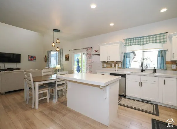 Kitchen featuring white cabinetry, light-toned countertops, a stainless steel dishwasher, and wood-finish flooring