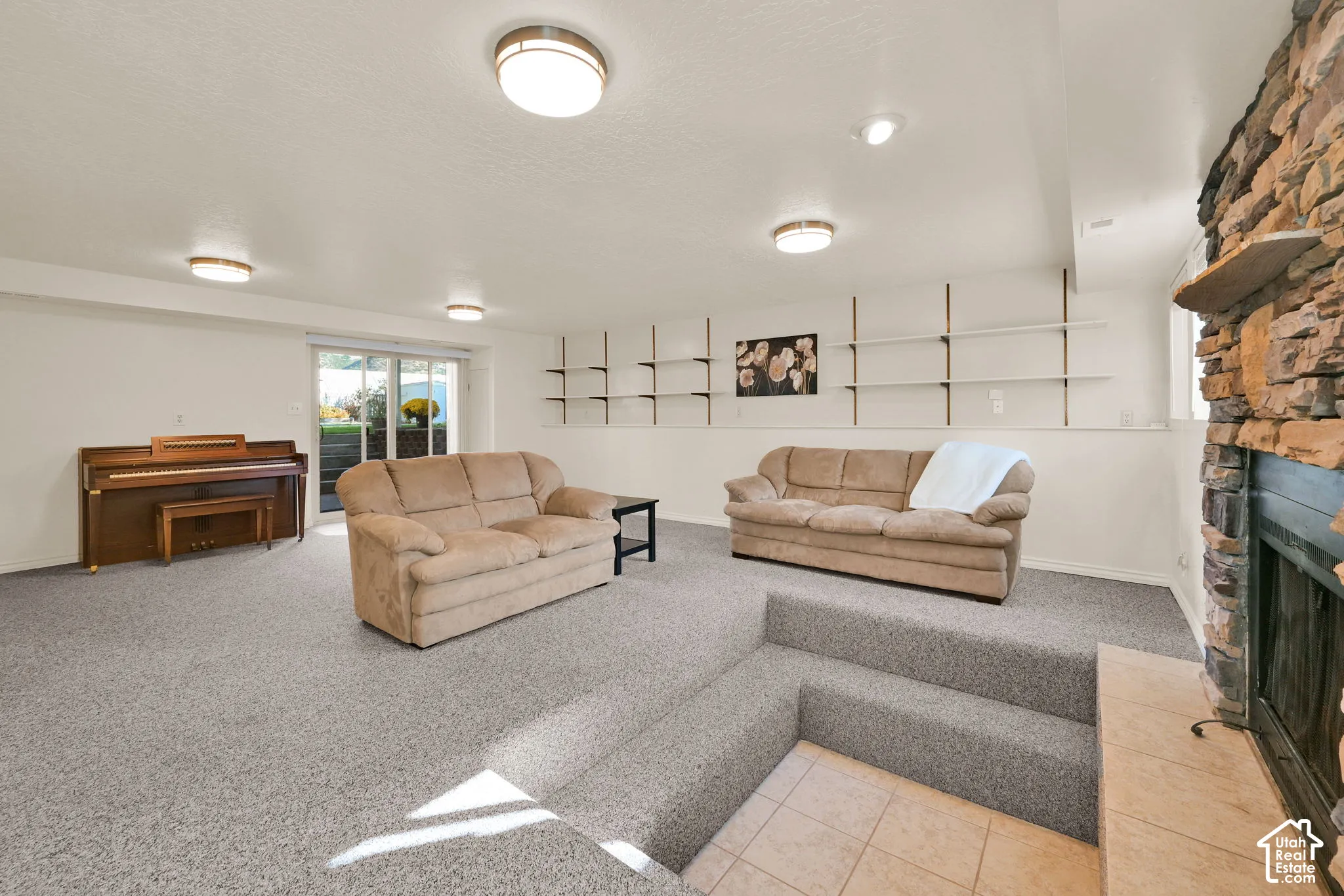 Basement living room. Carpeted lower-level living area with a stone-clad fireplace and hearth