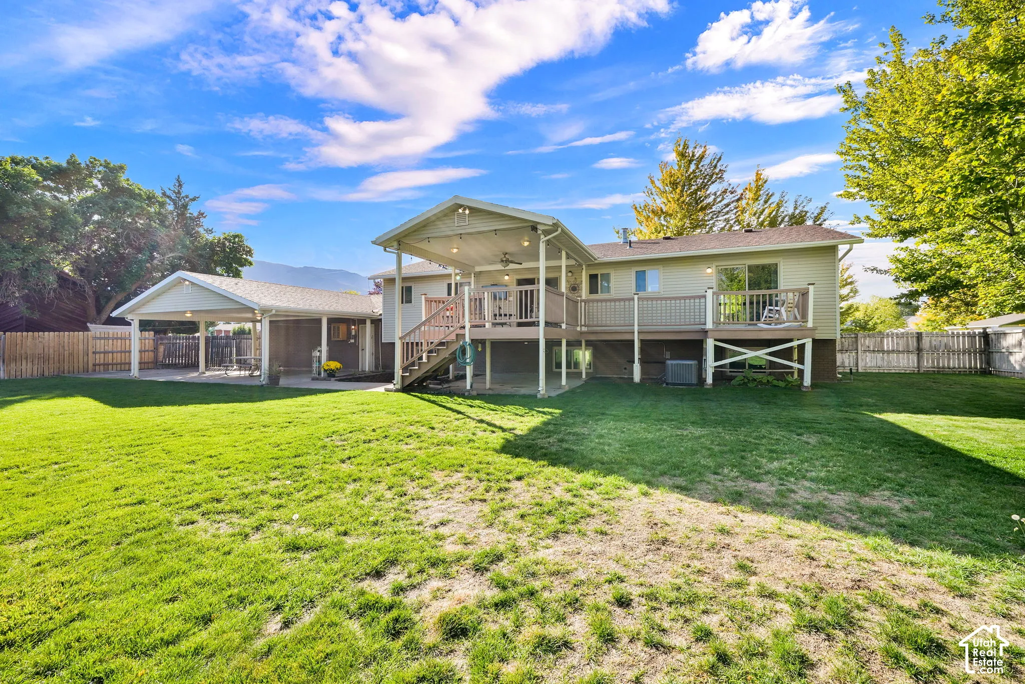 Expansive green lawn, deck with covered patio, carport, and wood privacy fencing
