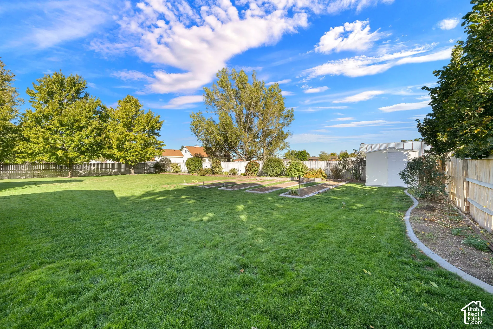 Expansive backyard with a manicured lawn, established trees, raised garden beds, and a storage shed