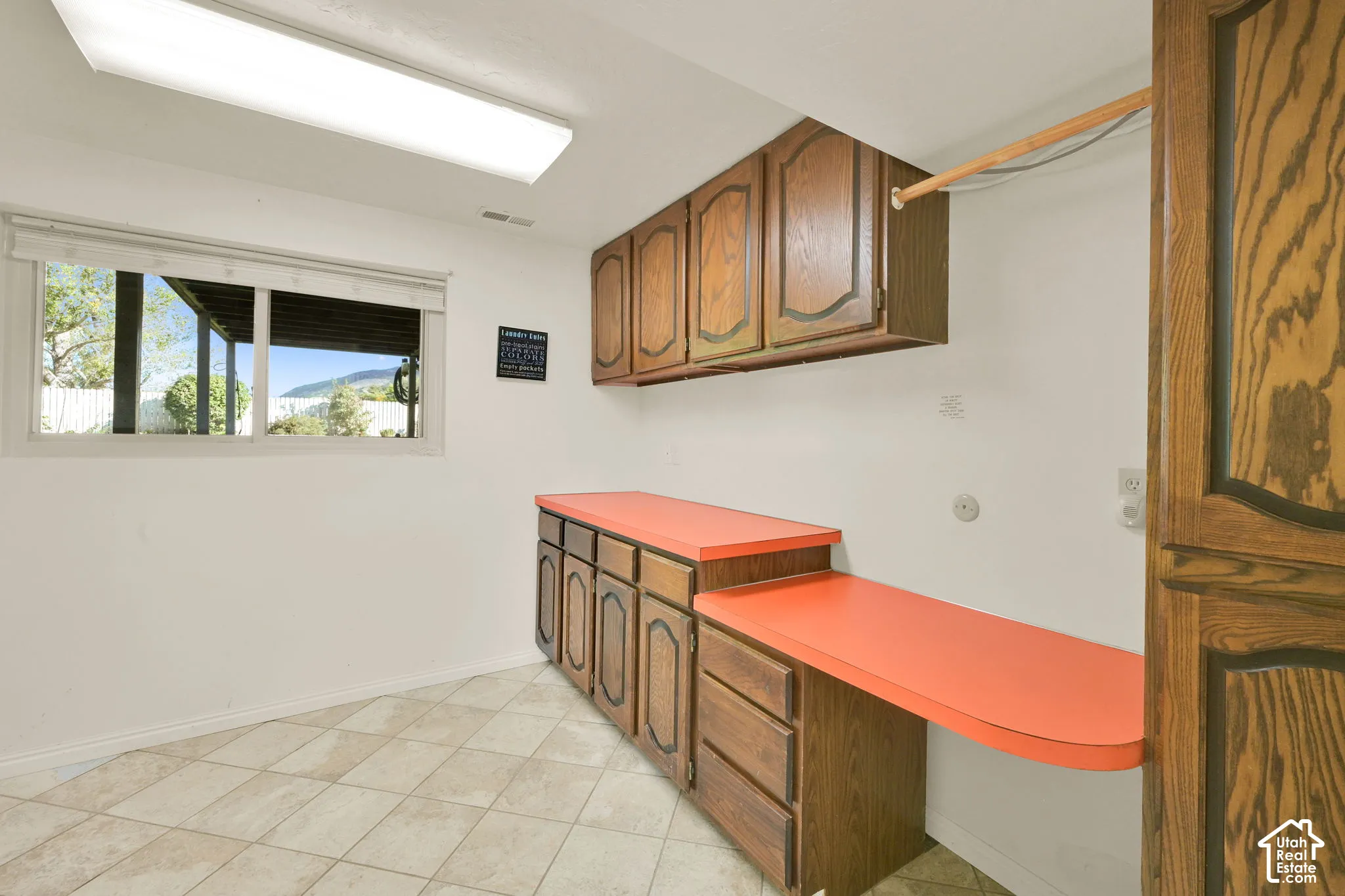 Laundry area featuring wood-finish cabinetry, orange laminate countertops, and a window providing natural light