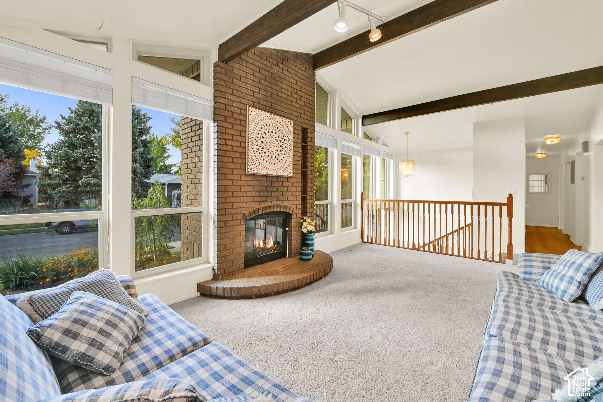 Vaulted ceiling with exposed wood beams, brick fireplace with hearth, wall of windows, and carpeted flooring