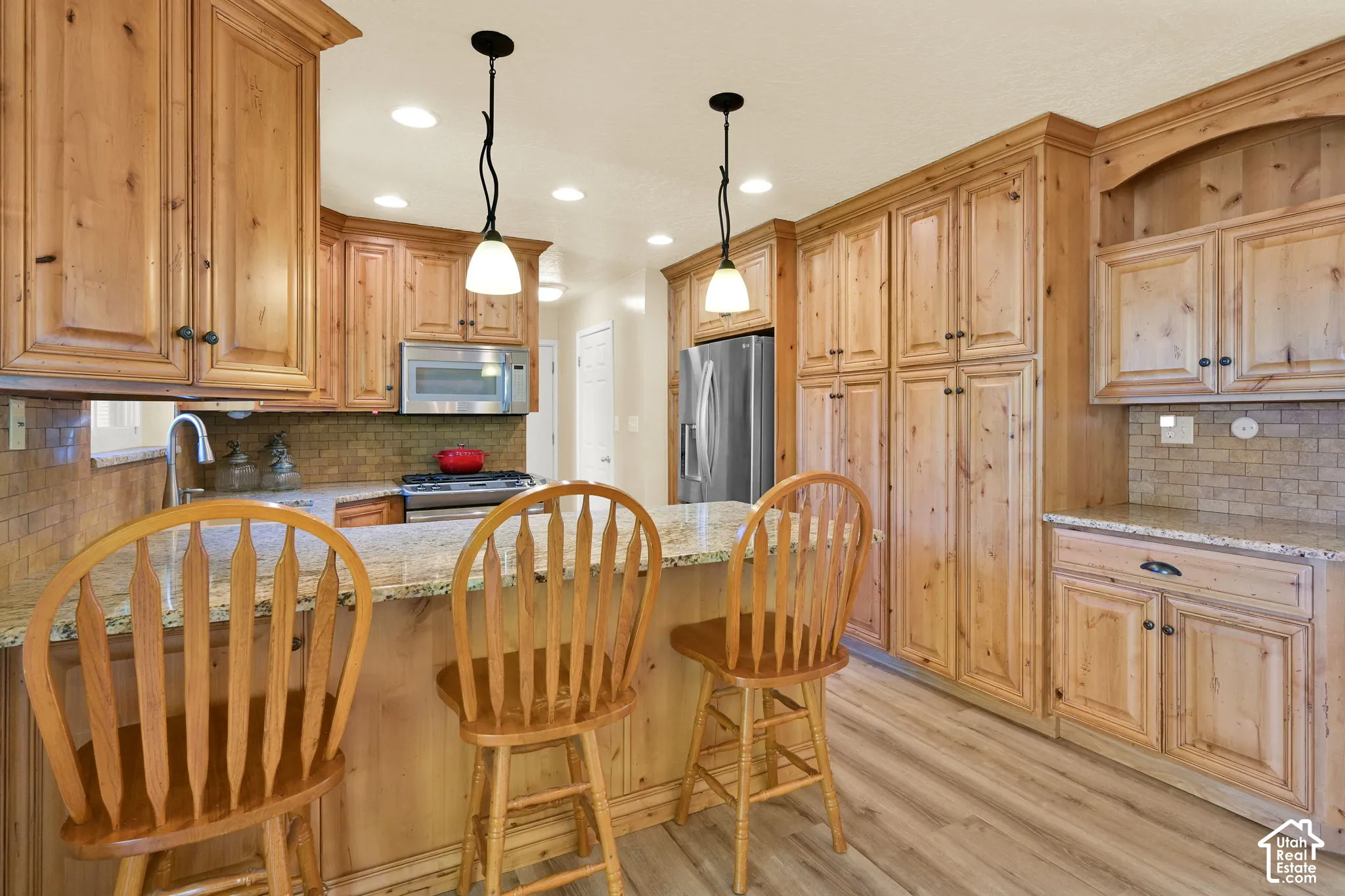 Light wood-finish cabinetry, granite countertops, tile backsplash, stainless steel appliances, and wood-finish flooring