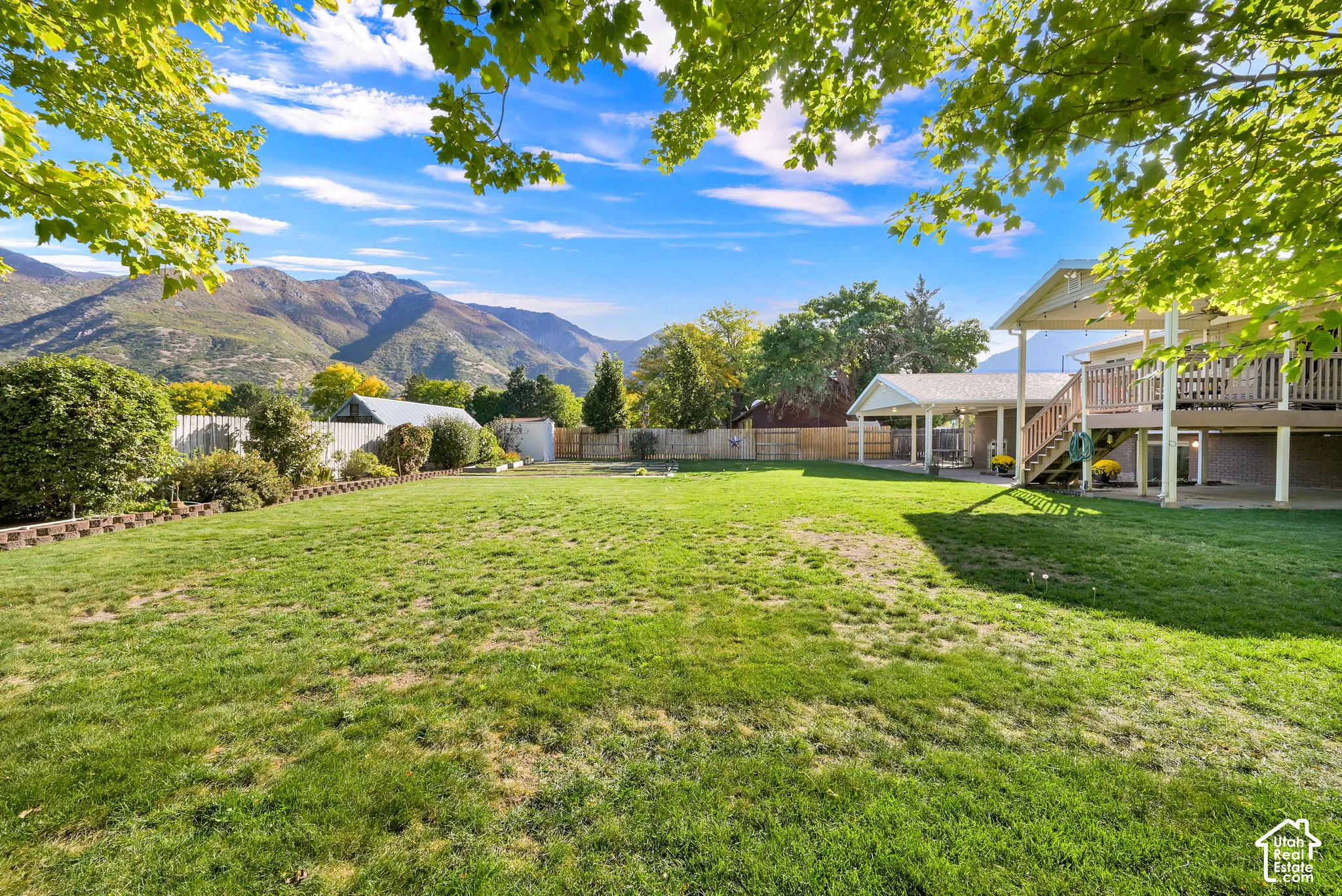Expansive backyard with a large grassy area, mature trees, and a wooden deck with stairs