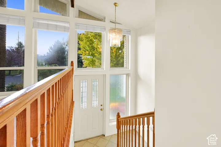 Entryway featuring a white door with divided lites, tiled flooring, wood-finish staircase railing, and a vaulted ceiling with a decorative chandelier
