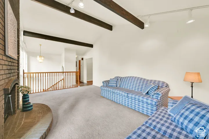 Vaulted ceiling with exposed wood beams, brick fireplace with a curved hearth, track lighting, light wood railing