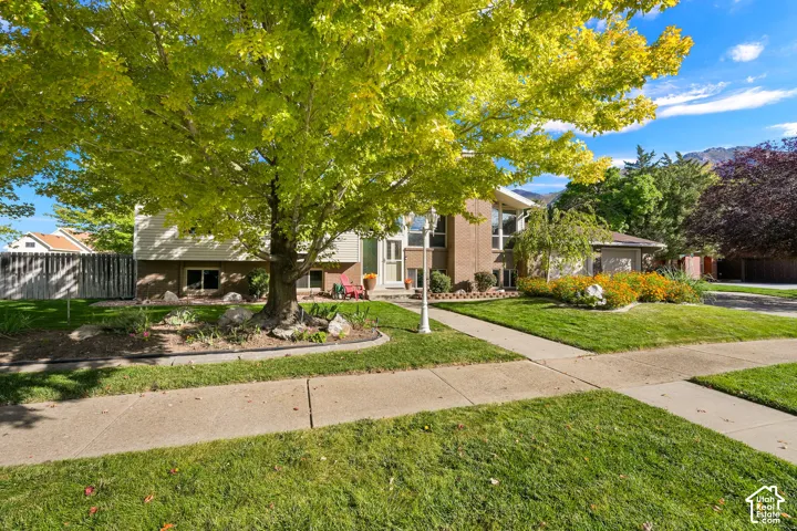 Brick exterior with vertical siding, mature trees, concrete sidewalks, and landscaped garden beds