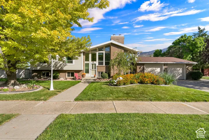 Split-level residence featuring a brick and vinyl siding exterior, multi-pane windows, a two-car garage, and a concrete sidewalk