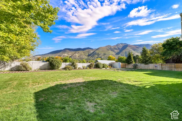 Expansive grass lawn with mountain backdrop, surrounded by mature trees and wood fencing