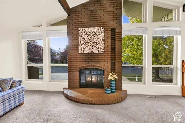 Vaulted ceiling featuring exposed wood beams, a brick fireplace with a curved hearth, built-in shelving, and large windows