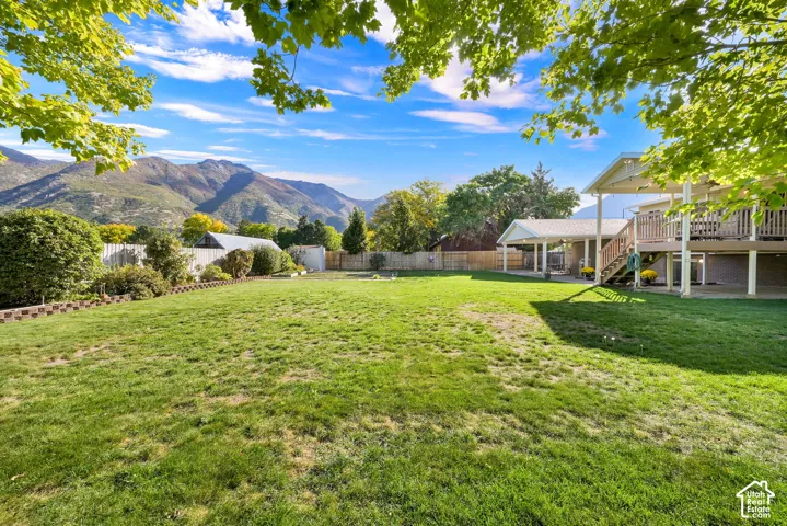 Expansive backyard with a large grassy area, mature trees, and a wooden deck with stairs