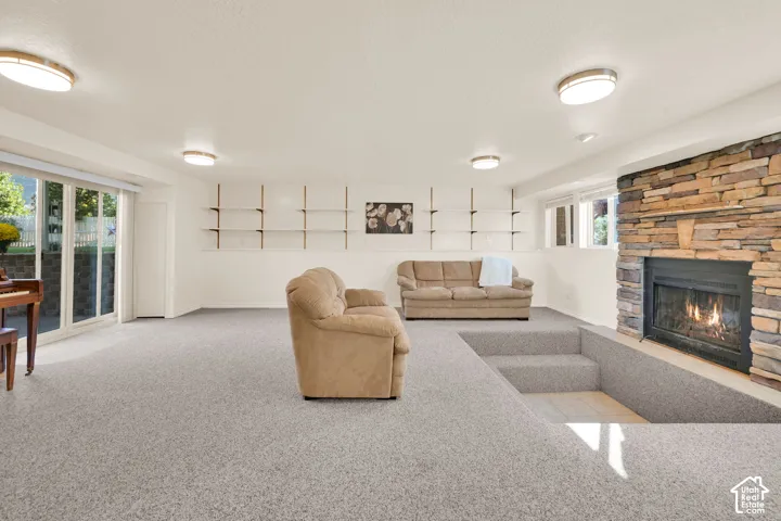 Basement living room with fireplace, recessed seating area, built-in shelving, light carpeting, and sliding glass doors to back yard