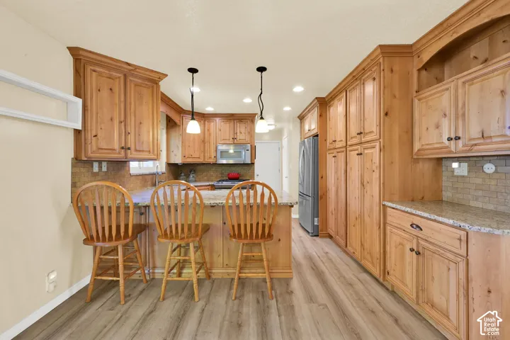 Kitchen featuring wood-finish flooring, wood cabinetry, granite countertops, a tiled backsplash, and stainless steel appliances