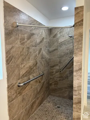 Shower featuring full-height tiled walls, a tiled floor with hexagonal mosaic, and two grab bars