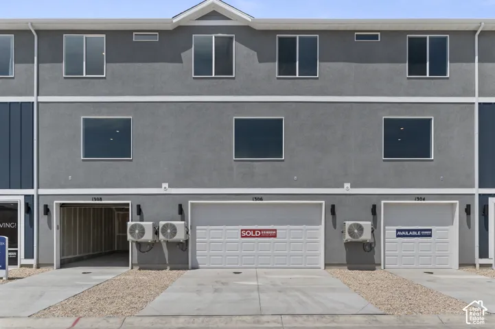 Gray stucco exterior with white trim, multiple windows, and individual garage entrances