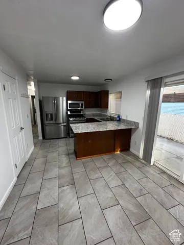 Kitchen featuring tile flooring, stone-patterned countertops, wood cabinetry, stainless steel refrigerator, and a sliding glass door