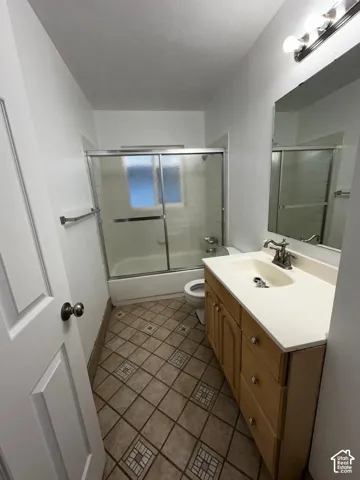 Bathroom featuring wood-finish cabinetry, integrated countertop with sink, sliding glass shower enclosure, and tile flooring with decorative inserts