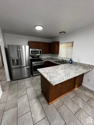 Kitchen featuring stone-finish countertops, dark wood-finish cabinetry, stainless steel appliances, and large-format tile flooring
