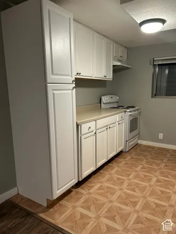 White cabinetry featuring extended pantry storage, neutral countertops, white range with integrated hood, and patterned flooring