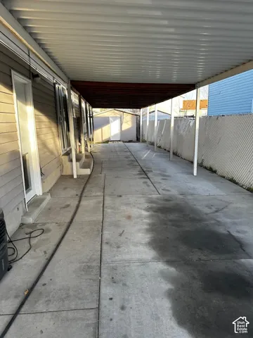 Covered carport featuring a metal roof, concrete parking pad, and detached storage structure enclosed by a perimeter fence