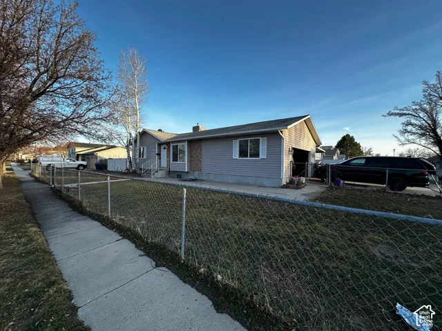 Single-level exterior featuring light-toned horizontal siding, a masonry chimney, an attached garage, and a chain-link fenced yard