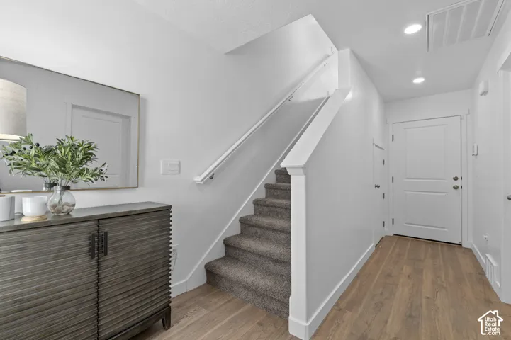 Wood-finish flooring, staircase with carpeted treads, white panel doors, and recessed lighting