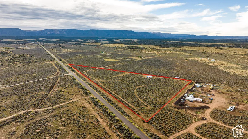 Expansive vacant lot with defined boundaries, bordering a paved road, and featuring distant mountain ranges
