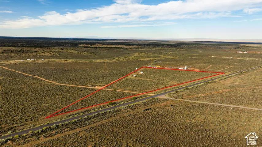 Expansive undeveloped land with a paved road frontage, characterized by natural vegetation and a clear, open sky