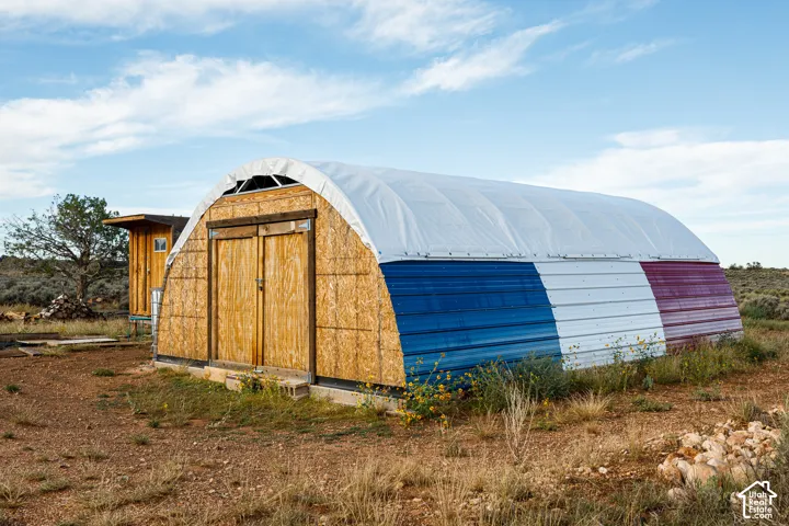 Quonset hut style structure with plywood double doors, upper transom window, and metal siding with painted sections